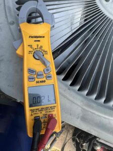 Clamp meter testing an outdoor AC condenser fan
